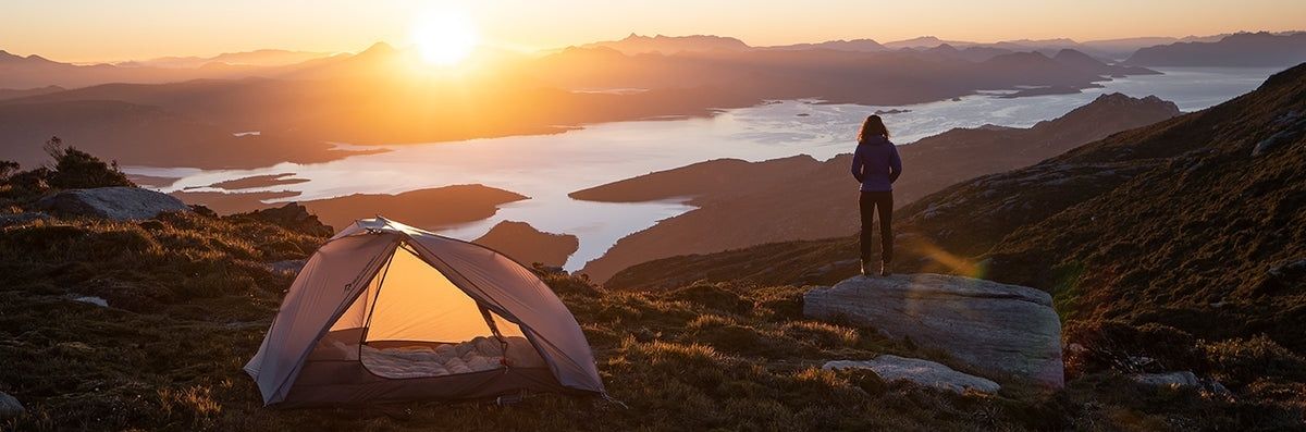 Telt og turgåer ved fjellvann i solnedgang